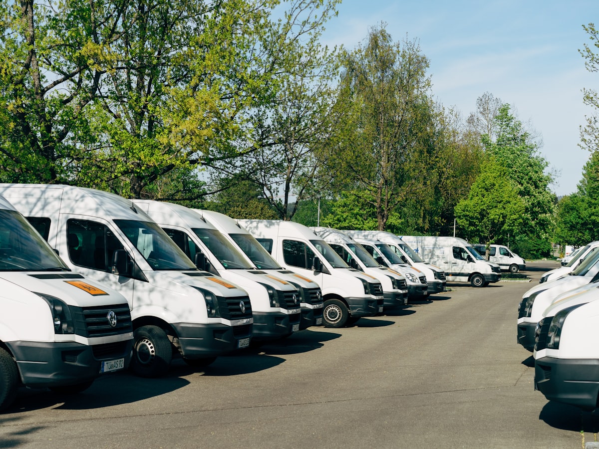 A row of white fleet vans parked under trees